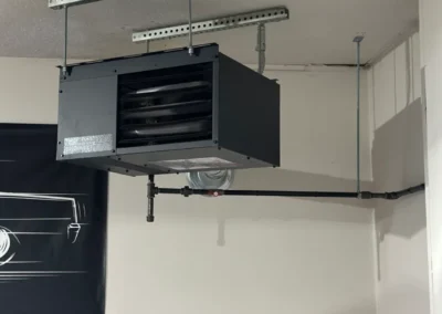 A gas water heater installed in a garage, showcasing its metallic exterior and connected pipes.